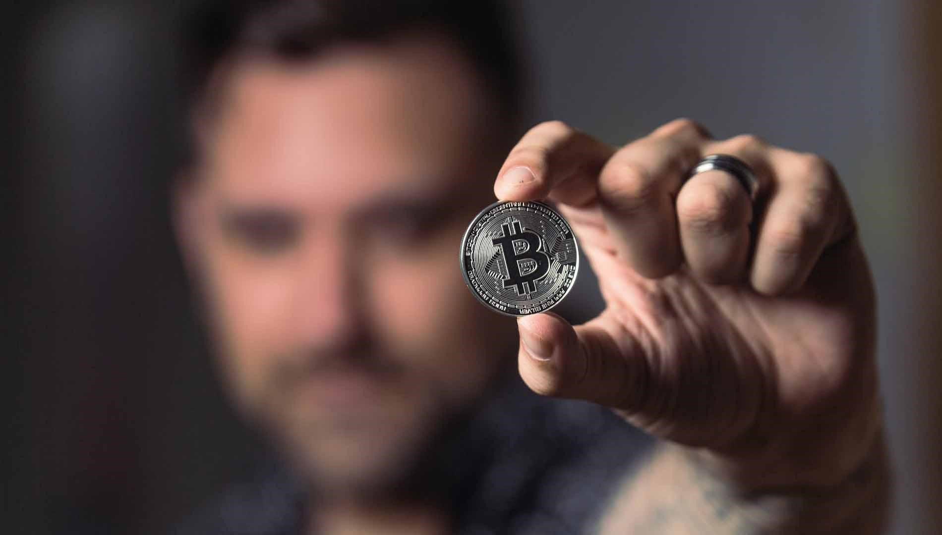 A man holding a silver coin with the bitcoin logo on it
