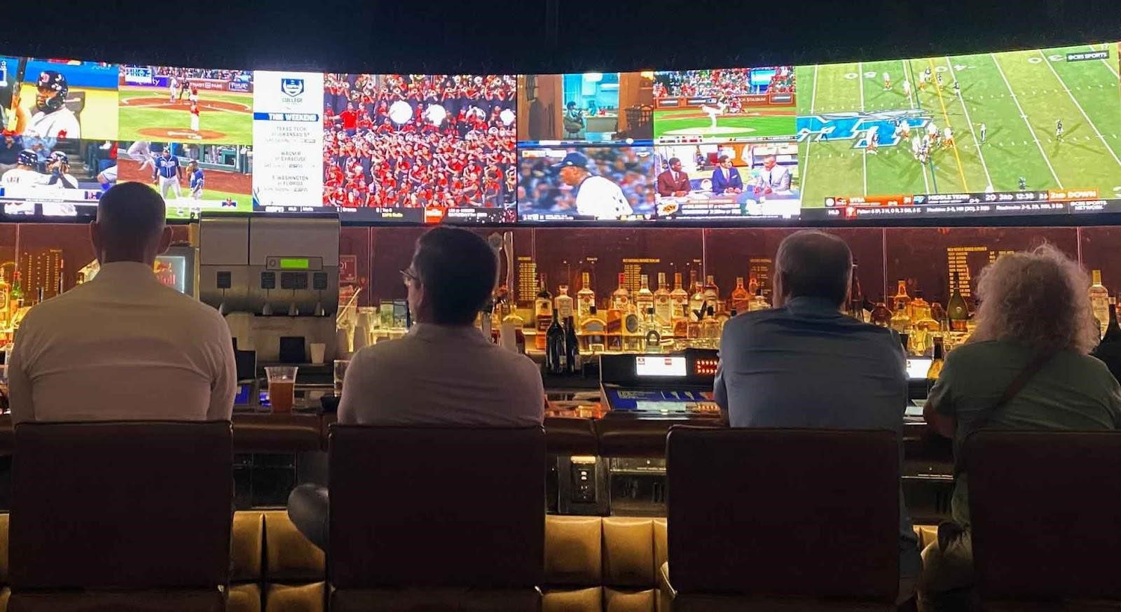 Image of four people sitting in a sportsbook in front of the bar